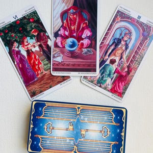 May include: Three tarot cards with colorful illustrations and text in multiple languages. The cards are laid out in a row on a white surface. The cards are from the Rider-Waite tarot deck.
