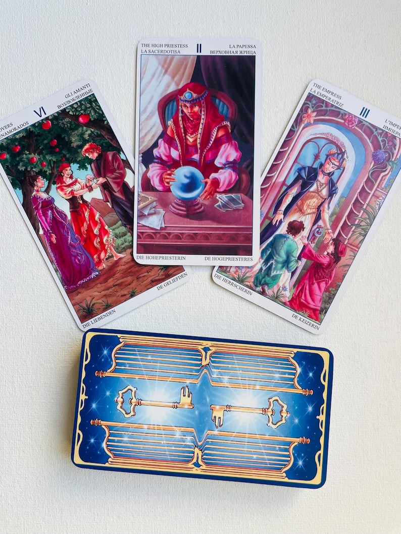 May include: Three tarot cards with colorful illustrations and text in multiple languages. The cards are laid out in a row on a white surface. The cards are from the Rider-Waite tarot deck.
