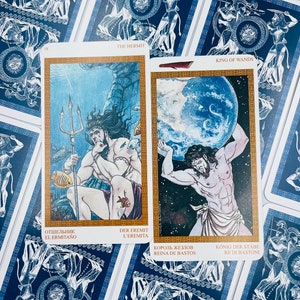 May include: Two tarot cards, The Hermit and King of Wands, with blue and gold borders. The Hermit card depicts a man with a trident standing in the ocean. The King of Wands card depicts a man holding a globe.