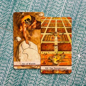 May include: Two tarot cards, Six of Wands and XIV The Temperance. The Six of Wands card features a man in a yellow tunic carving a stone with a tool. The Temperance card shows a city with a central building and a river.