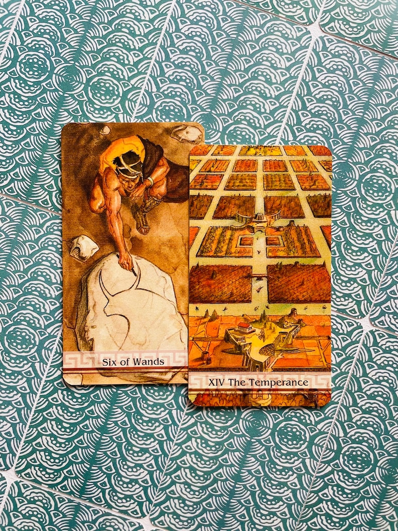 May include: Two tarot cards, Six of Wands and XIV The Temperance. The Six of Wands card features a man in a yellow tunic carving a stone with a tool. The Temperance card shows a city with a central building and a river.