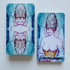 K&ouml;nnte beinhalten: Zwei Tarotkarten, eine mit blauem Hintergrund und einer Frau mit Maske und die andere mit rosa Hintergrund und einer Frau mit Maske und dem Text "II Die Hohepriesterin".