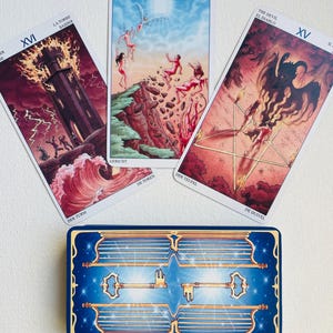 May include: Three tarot cards laid out on a white surface. The cards are from the Rider-Waite tarot deck. The cards are The Tower, Judgement, and The Devil. The cards are surrounded by a blue and gold key card.