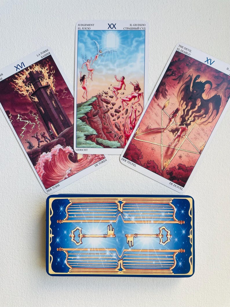 May include: Three tarot cards laid out on a white surface. The cards are from the Rider-Waite tarot deck. The cards are The Tower, Judgement, and The Devil. The cards are surrounded by a blue and gold key card.