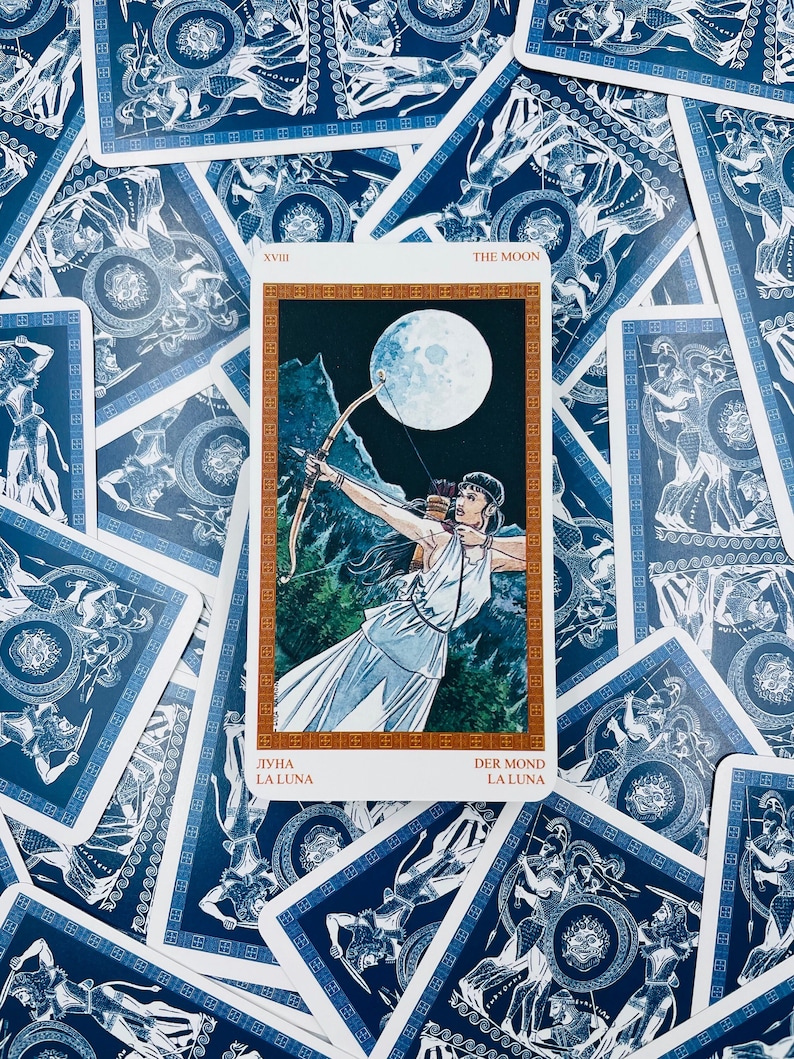 May include: The Moon tarot card from the Ancient Greek Tarot deck. The card features a woman with a bow and arrow standing in a forest with a full moon in the background. The card is surrounded by other tarot cards.