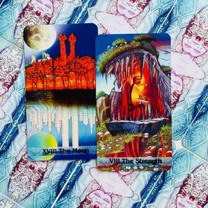 K&ouml;nnte beinhalten: Zwei Tarotkarten, Der Mond und Die St&auml;rke, mit bunten Illustrationen. Die Mondkarte zeigt eine Skyline mit einem Vollmond am Himmel. Die St&auml;rkekarten zeigt eine Person, die in einer H&ouml;hle mit einem L&ouml;wen sitzt.