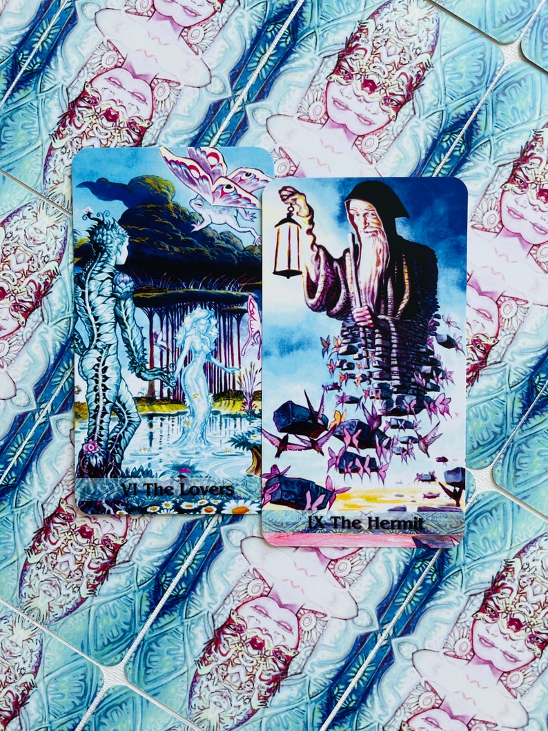 K&ouml;nnte beinhalten: Zwei Tarotkarten, Die Liebenden und Der Einsiedler, mit farbenfrohen Illustrationen. Die Karte Die Liebenden zeigt eine blaue und gr&uuml;ne Kreatur mit einem Schmetterling, w&auml;hrend die Karte Der Einsiedler eine Figur in einem violetten Gewand zeigt, die eine Laterne h&auml;lt.