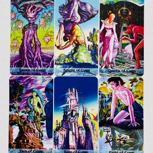 K&ouml;nnte beinhalten: Ein Satz von sechs Tarotkarten, die Szenen aus der Cups-Suite darstellen. Die Karten sind mit farbenfrohen, fantasievollen Bildern illustriert und tragen die Namen "Sieben der Kelche", "Ritter der Kelche", "K&ouml;nigin der Kelche", "Zwei der Kelche", "K&ouml;nig der Kelche" und "Acht der Kelche".
