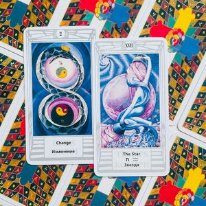 Pu&ograve; includere: Due carte dei tarocchi, una con un serpente e il numero 2, l'altra con una figura che tiene una stella e il numero XVII. Le carte sono bianche con bordi argentati e hanno testo in inglese e russo.