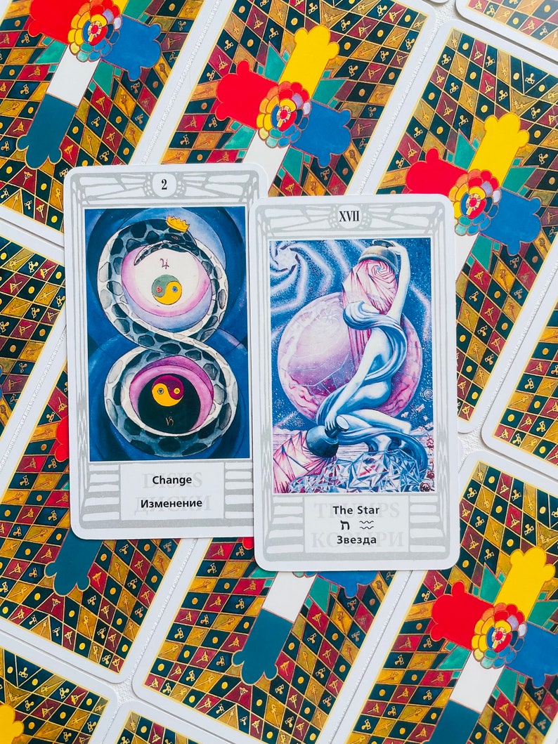 Pu&ograve; includere: Due carte dei tarocchi, una con un serpente e il numero 2, l'altra con una figura che tiene una stella e il numero XVII. Le carte sono bianche con bordi argentati e hanno testo in inglese e russo.