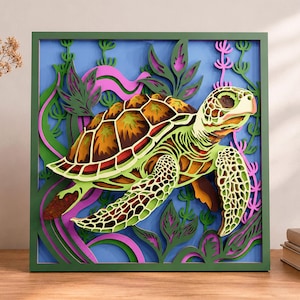 Puede incluir: Un arte de pared de madera multicapa que muestra una tortuga marina nadando entre plantas acuáticas. La tortuga tiene un caparazón marrón y bronceado con piel verde claro. El fondo es azul con detalles de algas verdes y rosas en un marco.