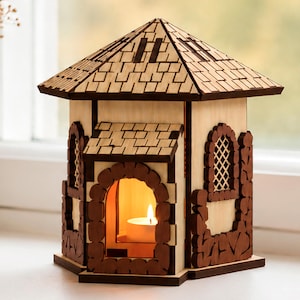 Puede incluir: Un portavelas de madera con forma de casa, con techo y paredes de color claro, que presenta marcos de ventana arqueados de color marrón oscuro y adornos decorativos. Una vela de té encendida es visible en el interior. La imagen incluye 1/8 in, 3 mm, 4 mm y Digital Download.