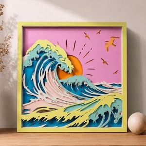 May include: A square, multi-layered paper art piece in a yellow frame depicting a stylized ocean wave in shades of blue, white, and yellow. The background is a solid pink with an orange sun and several small, dark brown birds flying in the sky.