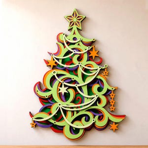 May include: A multi-layered wooden wall decoration shaped like a Christmas tree. The design features intricate, swirling cutouts in bright lime green, layered over orange, purple, and red sections. It is topped with a star and accented with small orange stars.