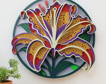 May include: A multi-layered paper artwork depicting a stylised lily flower. The flower has yellow, red, and purple petals with a white centre, set against a dark green circular background. Green leaves and red stamens add detail.