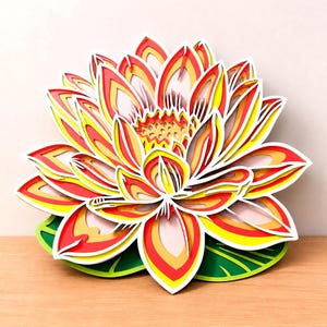 Könnte beinhalten: Ein mehrschichtiges, lasergeschnittenes Wandkunstobjekt, das eine blühende Lotusblume darstellt. Das Design zeigt leuchtende Blütenblätter in Rot-, Orange-, Gelb- und Weißtönen sowie einen detaillierten zentralen Blütenstempel.