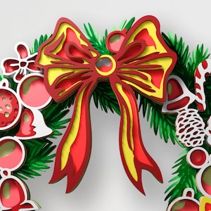 May include: A layered paper craft wreath featuring a large central red and yellow bow, green pine needles, red and white ornaments, a white pinecone, and a candy cane. The design uses stacked cutouts to create depth with red, yellow, and green colors.