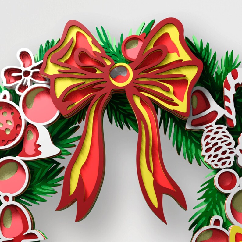 May include: A layered paper craft wreath featuring a large central red and yellow bow, green pine needles, red and white ornaments, a white pinecone, and a candy cane. The design uses stacked cutouts to create depth with red, yellow, and green colors.