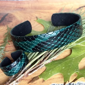 May include: A green and black snakeskin leather bracelet and ring set. The bracelet is wide and has a black suede backing. The ring is a simple band with a snakeskin design.