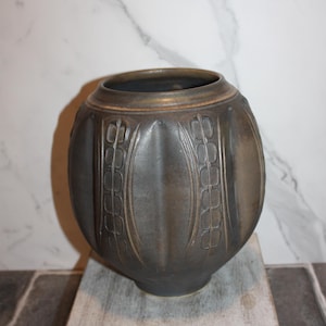 May include: A dark gray ceramic vase with a rounded body and a slightly flared rim. The vase features vertical, stylized leaf patterns and a textured surface. The vase is approximately 10 inches tall.