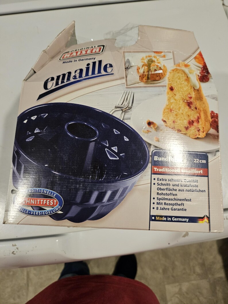 May include: A dark blue bundt cake pan in its original packaging. The box features the brand name "Kaiser emaille" and a picture of a slice of cake. The pan is 22 cm in diameter and made in Germany.