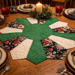 May include: A circular quilted table topper featuring a central green textured fabric surrounded by alternating panels of cream-colored fabric and black fabric with a floral pattern. The topper is placed on a wooden table with place settings.