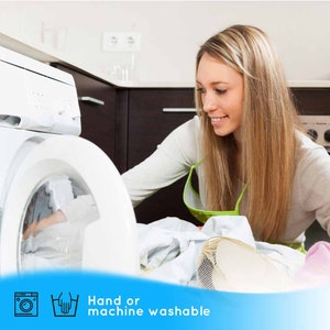 K&ouml;nnte beinhalten: Eine wei&szlig;e Waschmaschine mit einer Glast&uuml;r, in der ein wei&szlig;es Kleidungsst&uuml;ck zu sehen ist. Die Maschine steht in einer K&uuml;che, neben der eine Frau steht. Der Text "Handw&auml;sche oder Maschinenw&auml;sche" befindet sich auf einem blauen Banner am unteren Rand des Bildes.