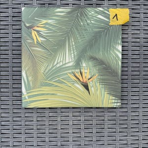 Könnte beinhalten: Quadratischer Leinwanddruck mit einem tropischen Palmenblatt-Design in Grün- und Gelbtönen. Das Kunstwerk zeigt eine Paradiesvogelblume. Ein gelber Haftzettel mit der Nummer "1" ist oben rechts angebracht.