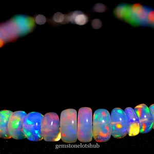 Puede incluir: Una hebra de cuentas de ópalo iridiscente en una variedad de colores, incluyendo azul, verde, rojo y amarillo. Las cuentas están enhebradas en una cadena de plata y están dispuestas en un patrón circular.
