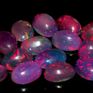 May include: A collection of oval-shaped opals in various shades of pink, purple, and blue. The opals are iridescent and have a shimmering effect.