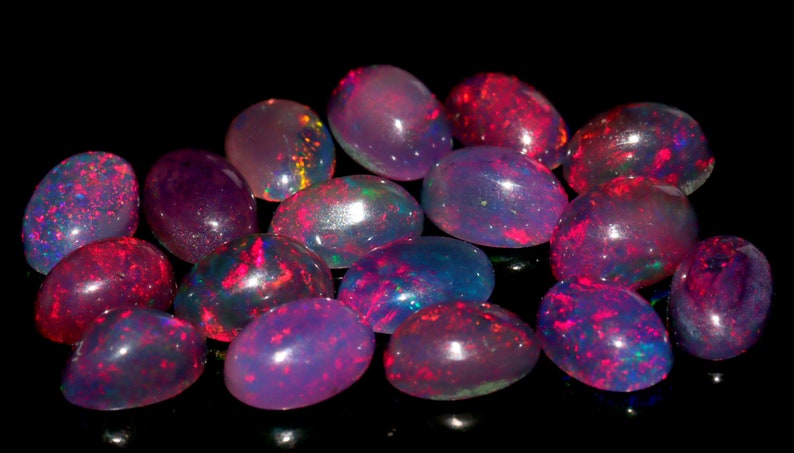 May include: A collection of oval-shaped opals in various shades of pink, purple, and blue. The opals are iridescent and have a shimmering effect.