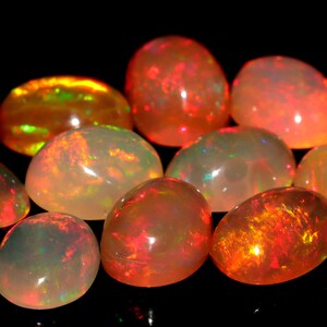 May include: A collection of ten oval-shaped opals with a variety of colors, including white, orange, red, and green. The opals are iridescent and have a smooth, polished finish.