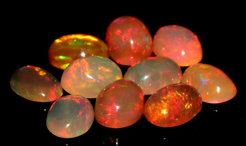 May include: A collection of ten oval-shaped opals with a variety of colors, including white, orange, red, and green. The opals are iridescent and have a smooth, polished finish.
