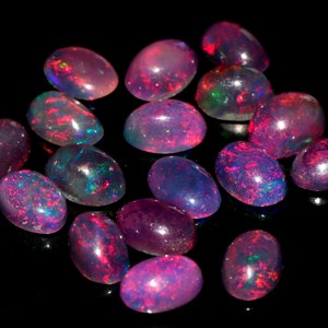 May include: A collection of oval-shaped, iridescent opals in shades of pink, purple, and blue. The opals are arranged on a black background.
