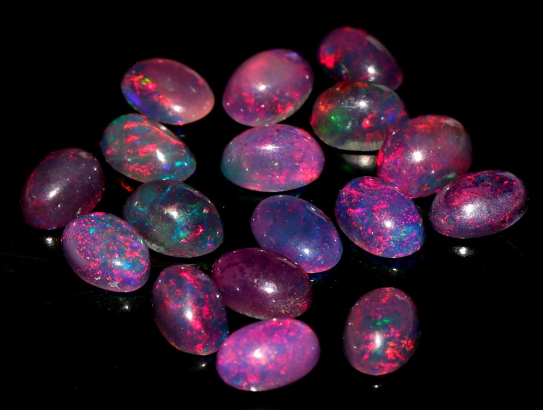 May include: A collection of oval-shaped, iridescent opals in shades of pink, purple, and blue. The opals are arranged on a black background.