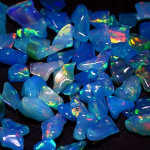 Może przedstawiać: Kolekcja niebieskich opali z iryzującymi refleksami koloru. Opale mają różne kształty i rozmiary i są rozrzucone na czarnej powierzchni.