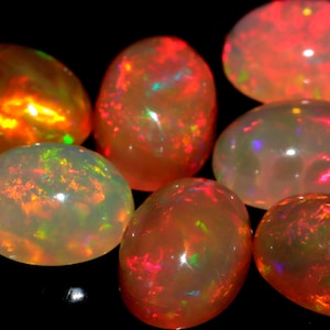 May include: A collection of oval-shaped opals with a variety of colors, including red, orange, green, and white. The opals are iridescent and have a smooth, polished finish.