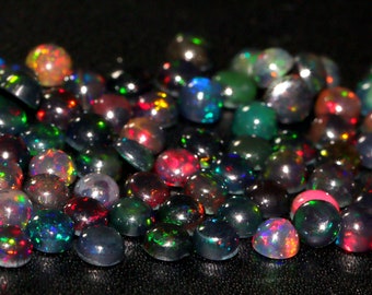 May include: A collection of black opal cabochons in various sizes and shades of green, red, and blue. The opals are iridescent and have a high shine.