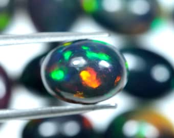 May include: A black opal gemstone with green and orange iridescence. The opal is round and has a smooth, polished surface.