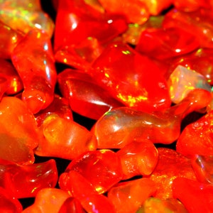 Puede incluir: Primer plano de un montón de piedras preciosas de ópalo rojo y naranja. Las piedras son lisas y brillantes, con un ligero brillo iridiscente.