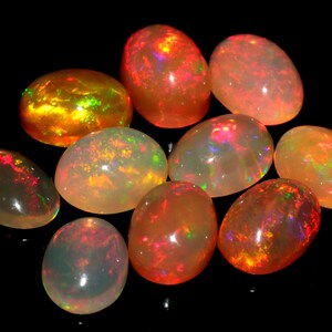 May include: A collection of ten oval-shaped opals with a variety of colors, including orange, red, and white. The opals are iridescent and have a smooth, polished finish.