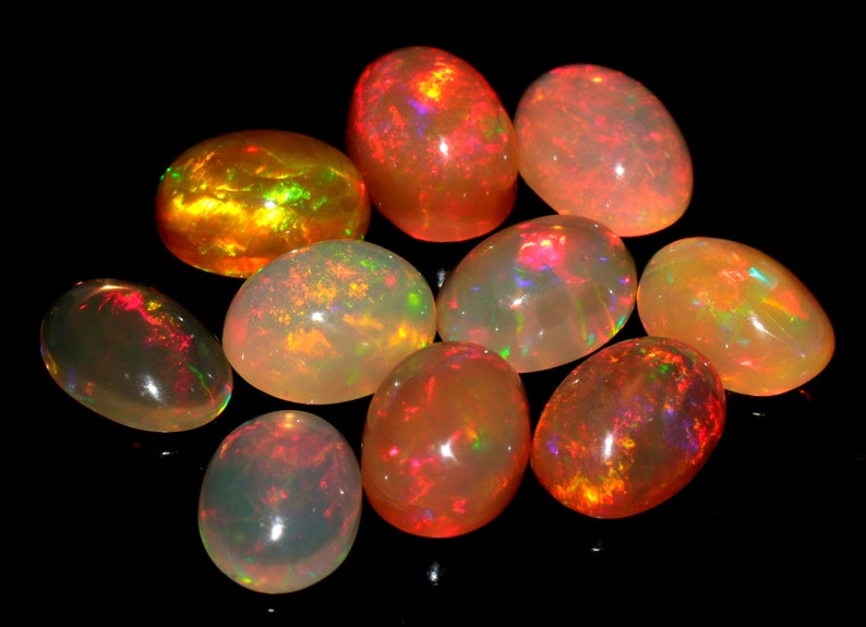 May include: A collection of ten oval-shaped opals with a variety of colors, including orange, red, and white. The opals are iridescent and have a smooth, polished finish.