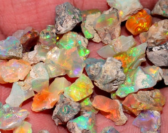 Puede incluir: Una colección de piedras de ópalo en bruto en varios tonos de blanco, naranja y verde. Las piedras son iridiscentes y tienen un aspecto natural y en bruto.