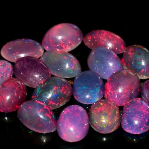 May include: A collection of oval-shaped opals in various shades of pink, purple, and blue. The opals are iridescent and have a shimmering effect.