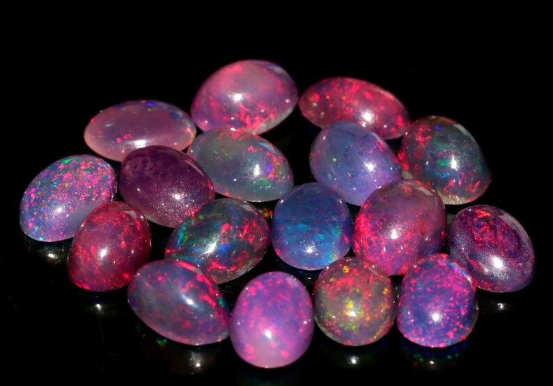 May include: A collection of oval-shaped opals in various shades of pink, purple, and blue. The opals are iridescent and have a shimmering effect.