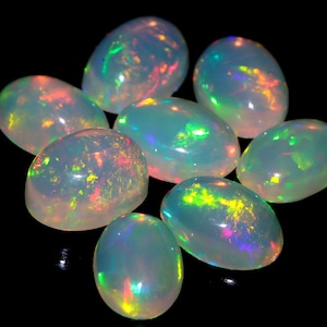 May include: A group of eight oval-shaped, iridescent opal gemstones. The opals are a pale white colour with flashes of green, blue, and red.