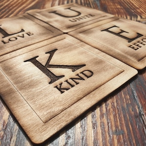 May include: Four wooden coasters with the letters L, U, K, and E, each with a word underneath: LOVE, UNITE, KIND, and EFFORT.