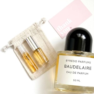 Pode incluir: Um frasco de perfume com tampa preta e rótulo branco que diz "BYREDO PARFUMS BAUDELAIRE EAU DE PARFUM 50 ML." Também estão presentes dois pequenos frascos de perfume e um cartão rosa de "obrigado".