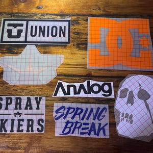 May include: A collection of iron-on patches featuring various logos and designs. The patches include a star, a skull, a logo with the text "UNION", a logo with the text "DC", a logo with the text "Analog", a logo with the text "SPRAY SKIERS", and a logo with the text "SPRING BREAK".