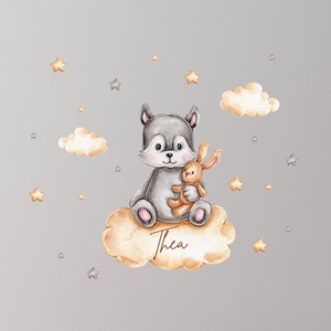 Peut inclure: Un animal gris et blanc avec un lapin brun dans ses bras est assis sur un nuage avec le nom Thea écrit dessus. L'arrière-plan est un mur gris avec des étoiles argentées et des nuages.